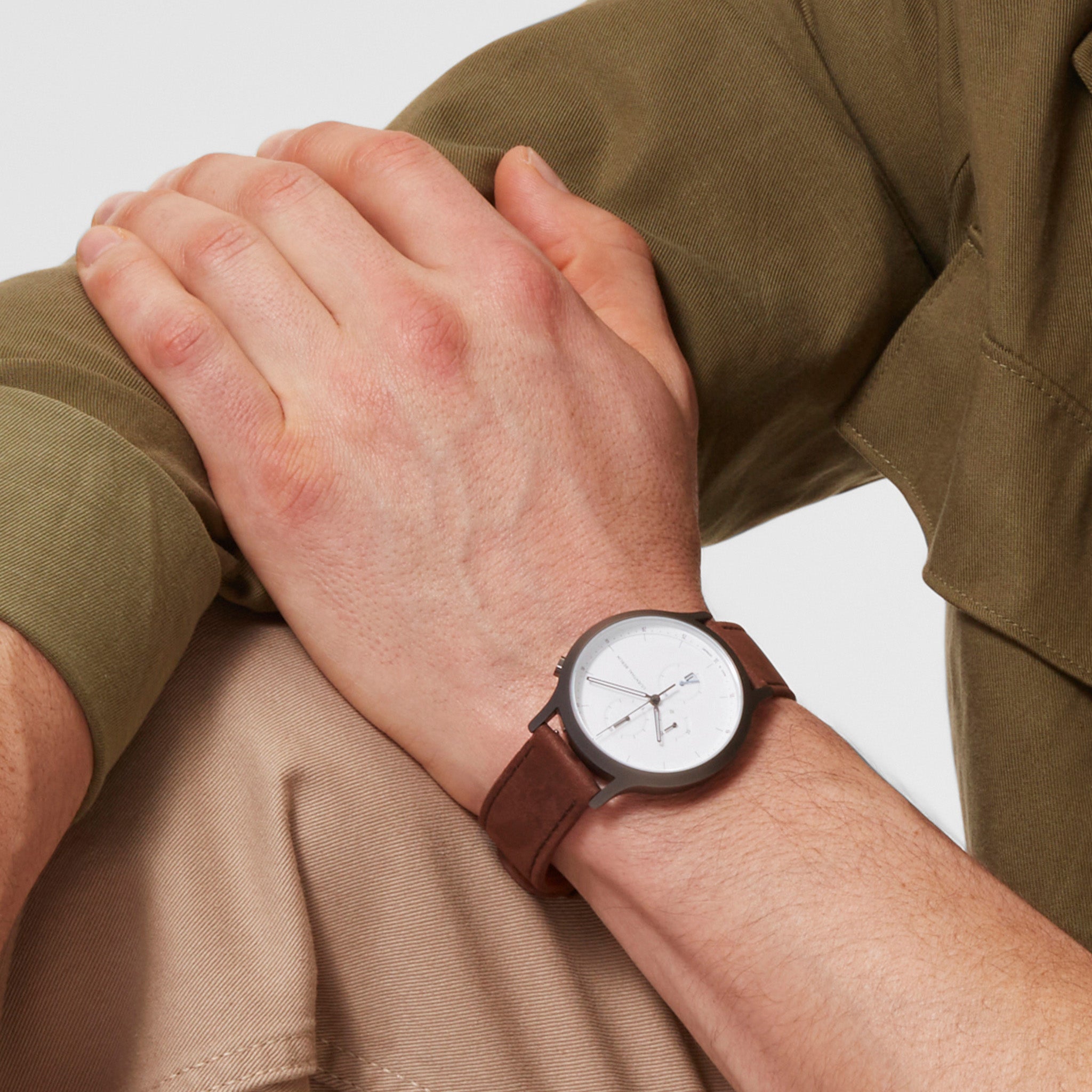 Minimalist wristwatch with white dial and brown leather strap on a person wearing khaki clothing