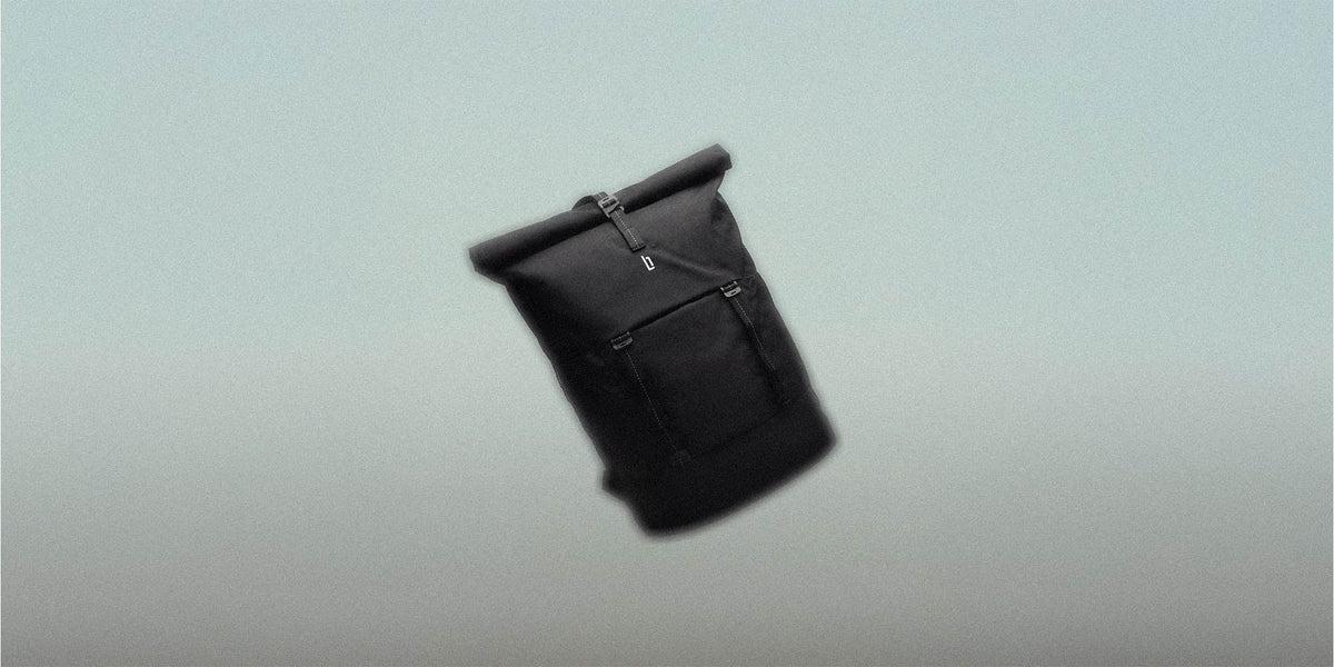 Black rolltop backpack with front pocket on a minimalist grey background