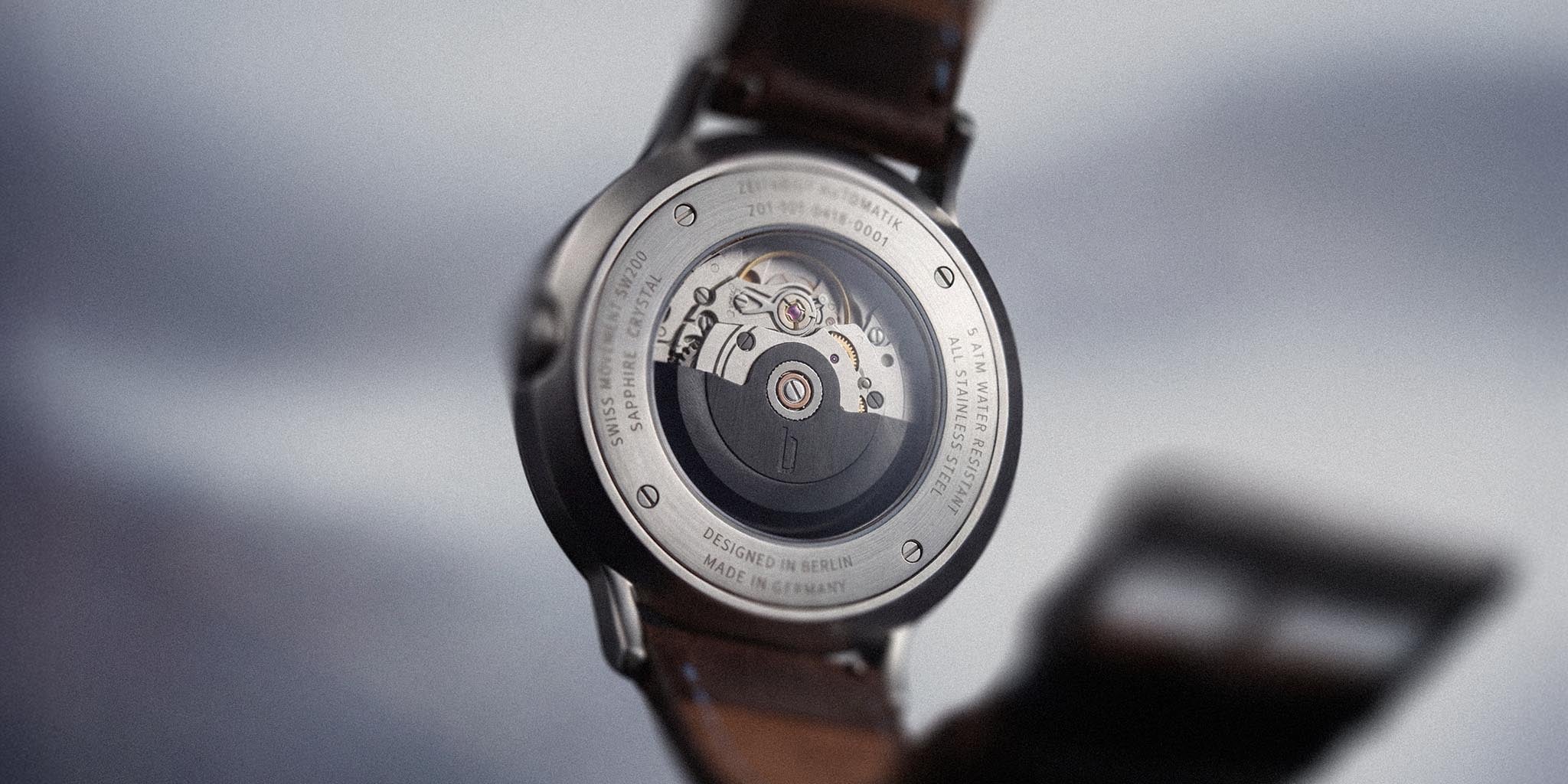 Close-up of automatic watch caseback with visible Swiss movement and brown leather strap
