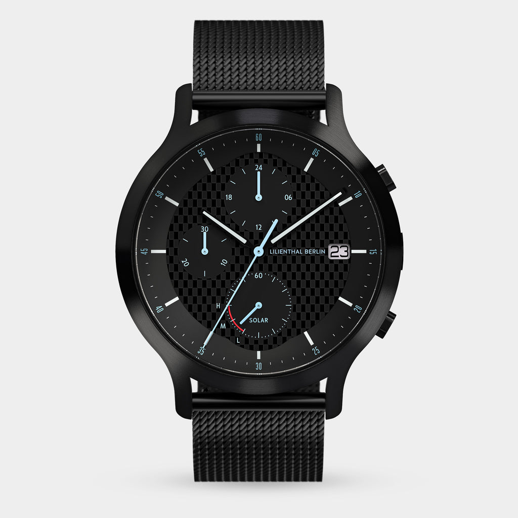 Black solar-powered chronograph watch with mesh strap, checkerboard dial, date display