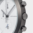 Close-up of a modern chronograph watch with white dial, three subdials, and metal pushers.