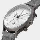 Minimalist silver chronograph watch with white dial and grey suede strap, close-up view
