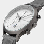 Minimalist silver chronograph watch with white dial and grey suede strap, close-up view