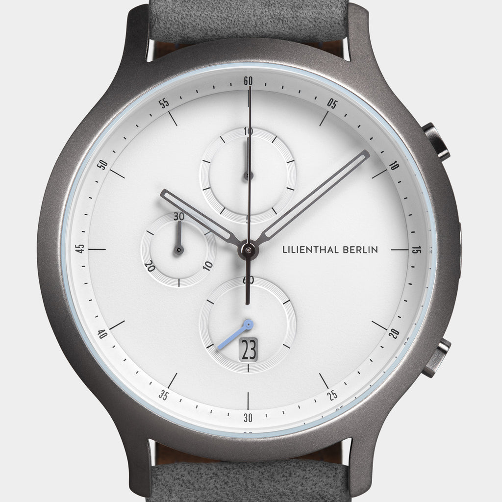 Minimalist silver chronograph watch with white dial, subdials, date display, and grey leather strap