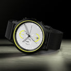Modern chronograph watch with black mesh strap, silver dial, and yellow accents on a dark background.