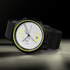 Modern chronograph watch with black mesh strap, silver dial, and yellow accents on a dark background.