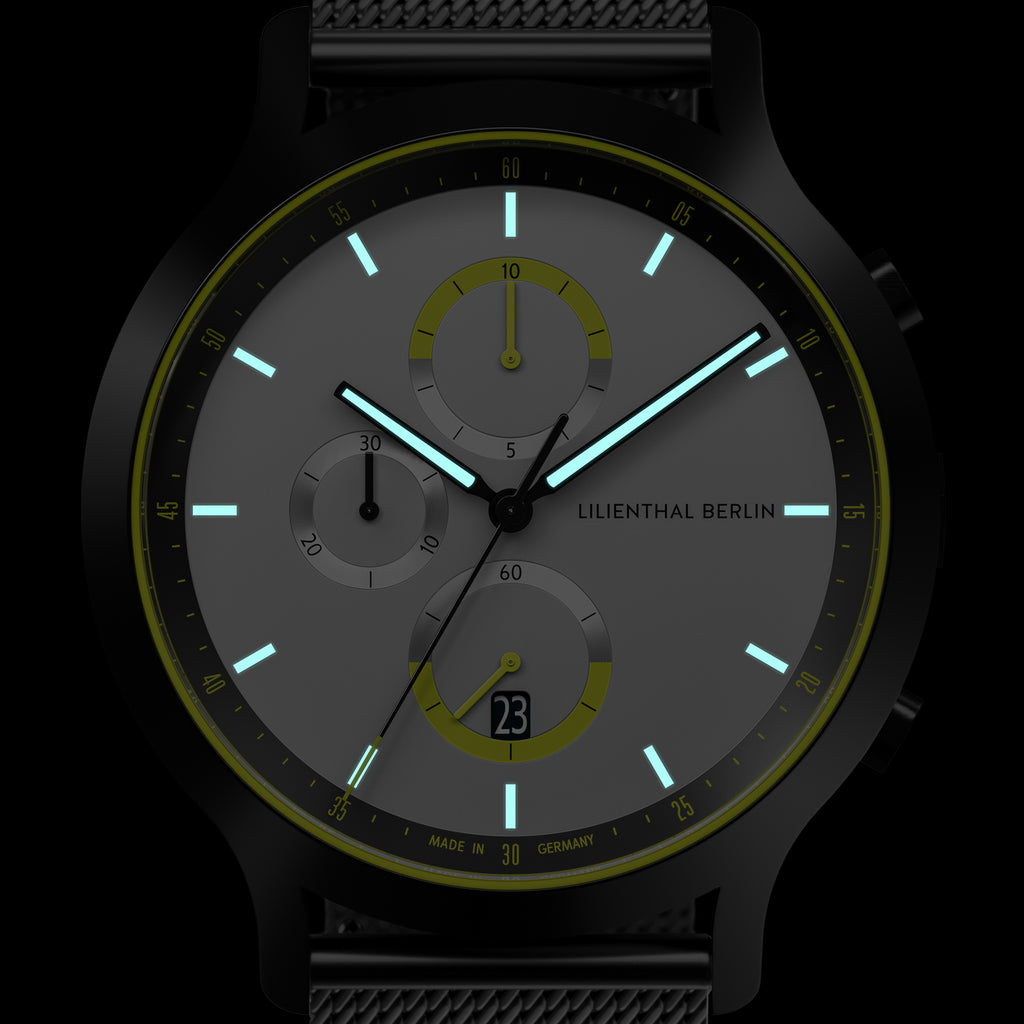 Modern chronograph watch with glowing hands, black case, and mesh band on dark background