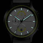 Modern chronograph watch with glowing hands, black case, and mesh band on dark background