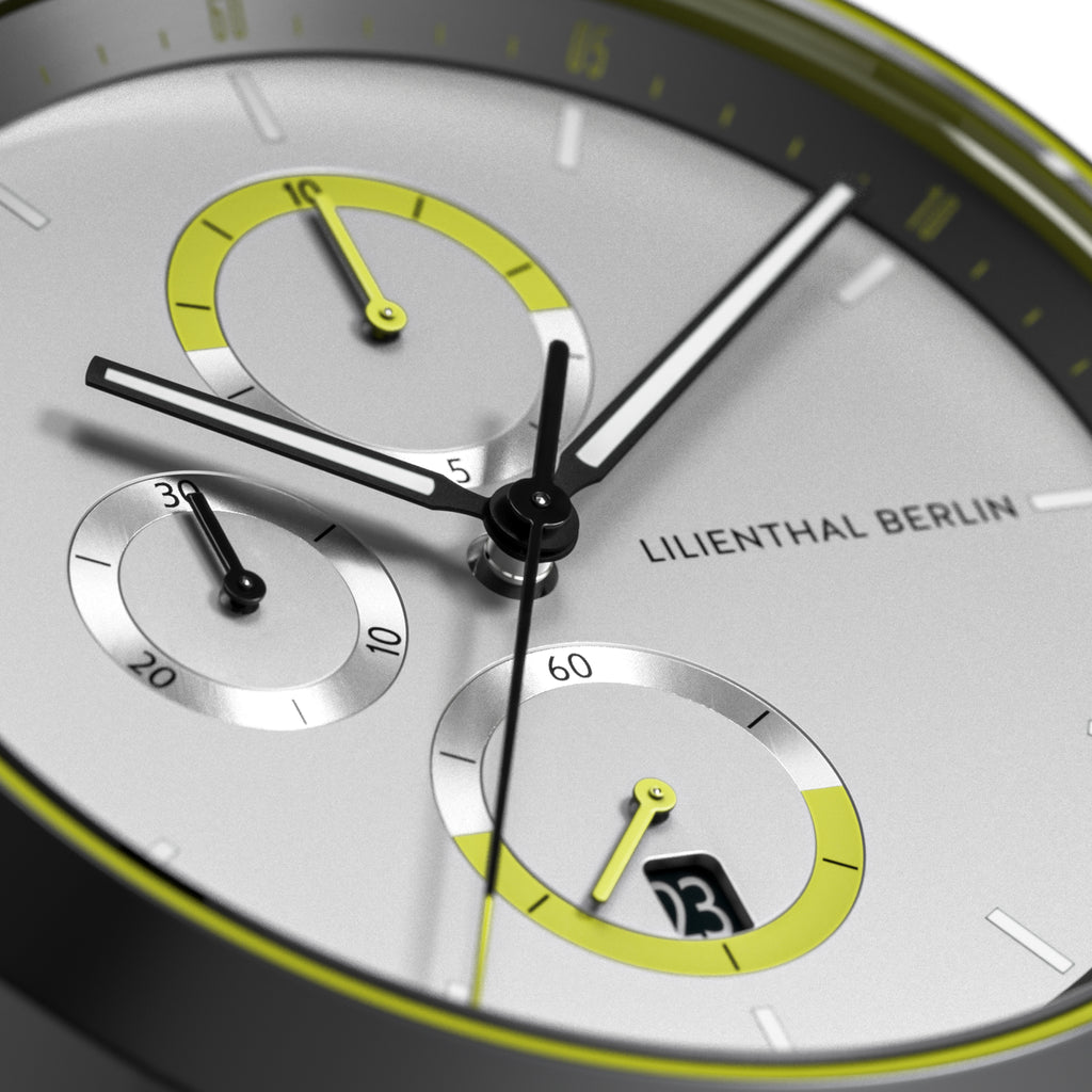 Close-up of a modern chronograph watch face with yellow accents and subdials on silver background.