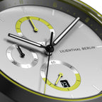Close-up of a modern chronograph watch face with yellow accents and subdials on silver background.