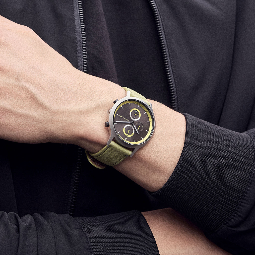 Modern wristwatch with black and yellow dial, green strap, worn on person's wrist in black jacket