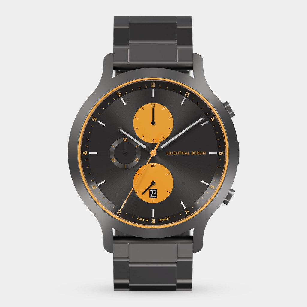 Modern chronograph watch with black metal band, black dial, and orange subdials.