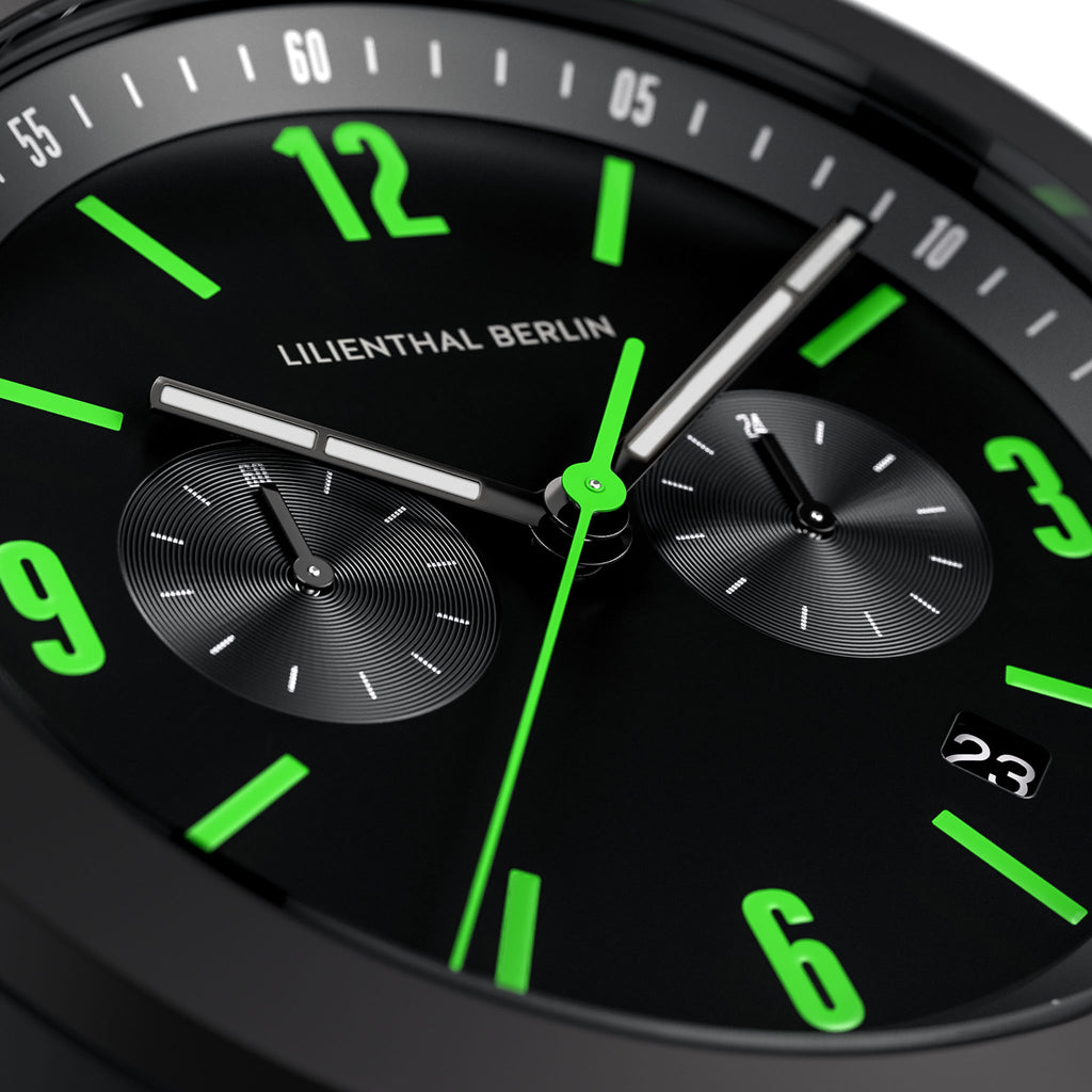 Close-up of modern black watch face with green numerals and chronograph subdials