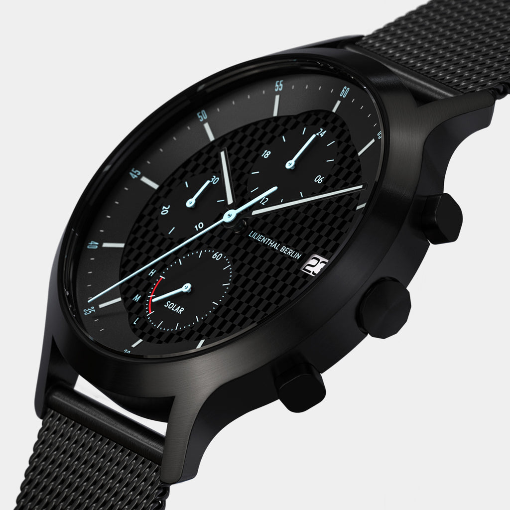 Black chronograph watch with mesh strap, textured dial, subdials, and date display