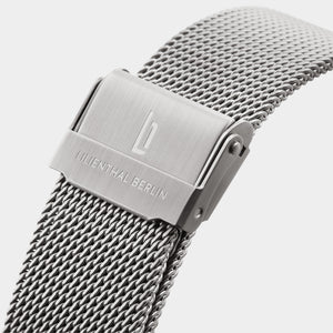 Close-up of stainless steel mesh watch strap with engraved clasp on white background