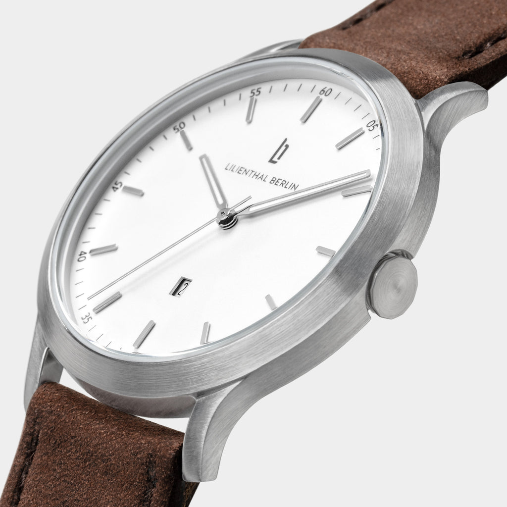 Minimalist silver wristwatch with white dial, brown leather strap, and date display
