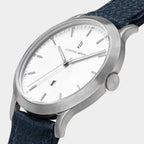 Minimalist silver wristwatch with white dial, date window, and dark textured leather strap