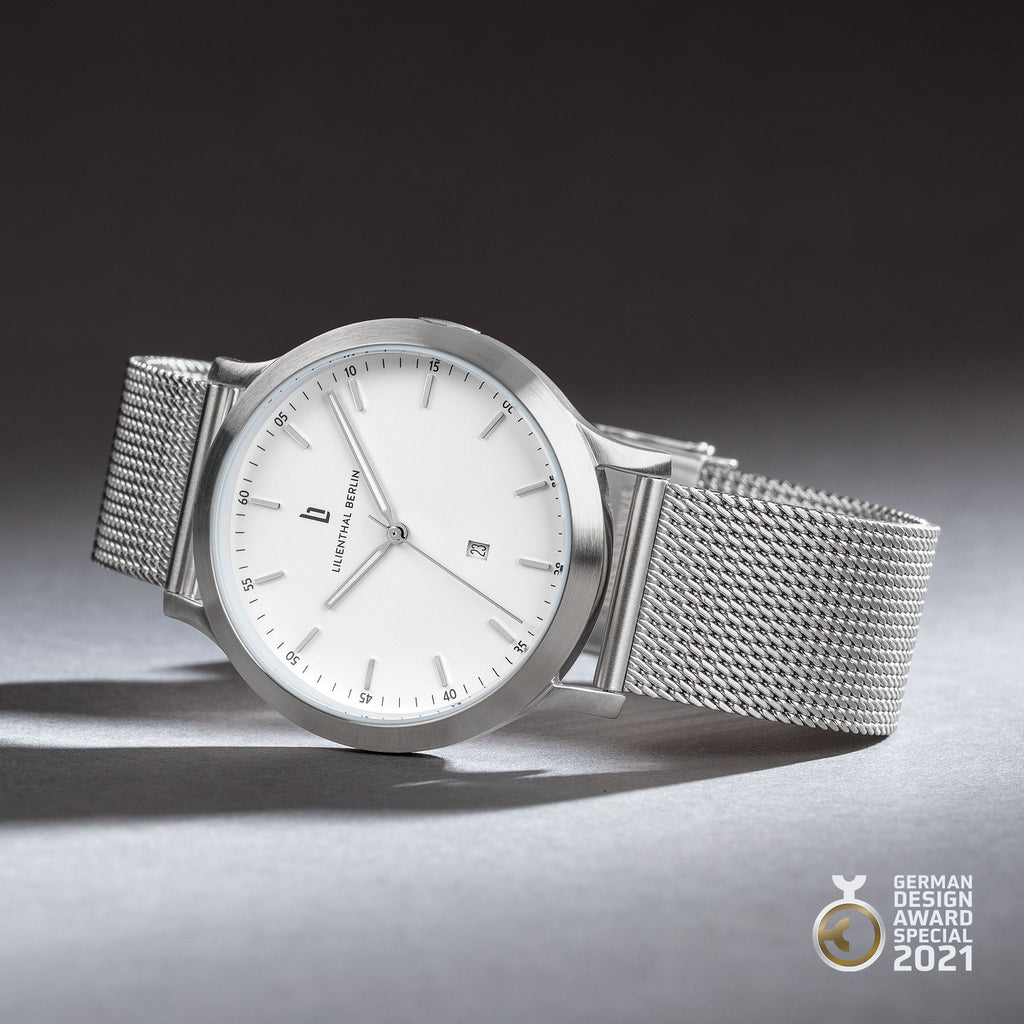 Minimalist silver mesh watch with white dial, date display, and German Design Award 2021 badge