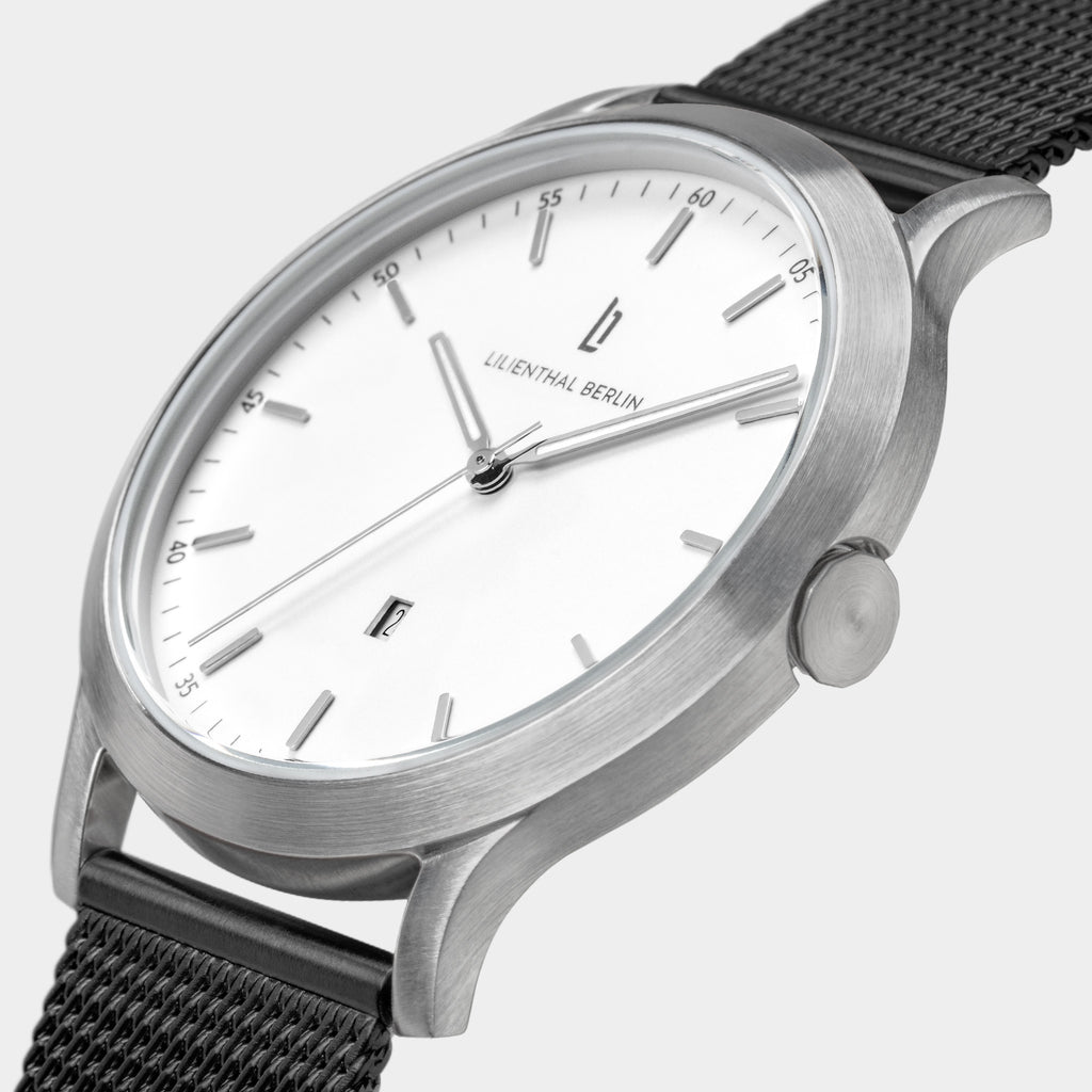 Minimalist silver wristwatch with white dial and black mesh strap, close-up view