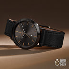 Minimalist black wristwatch with gold markers, black leather strap, date display, award badge