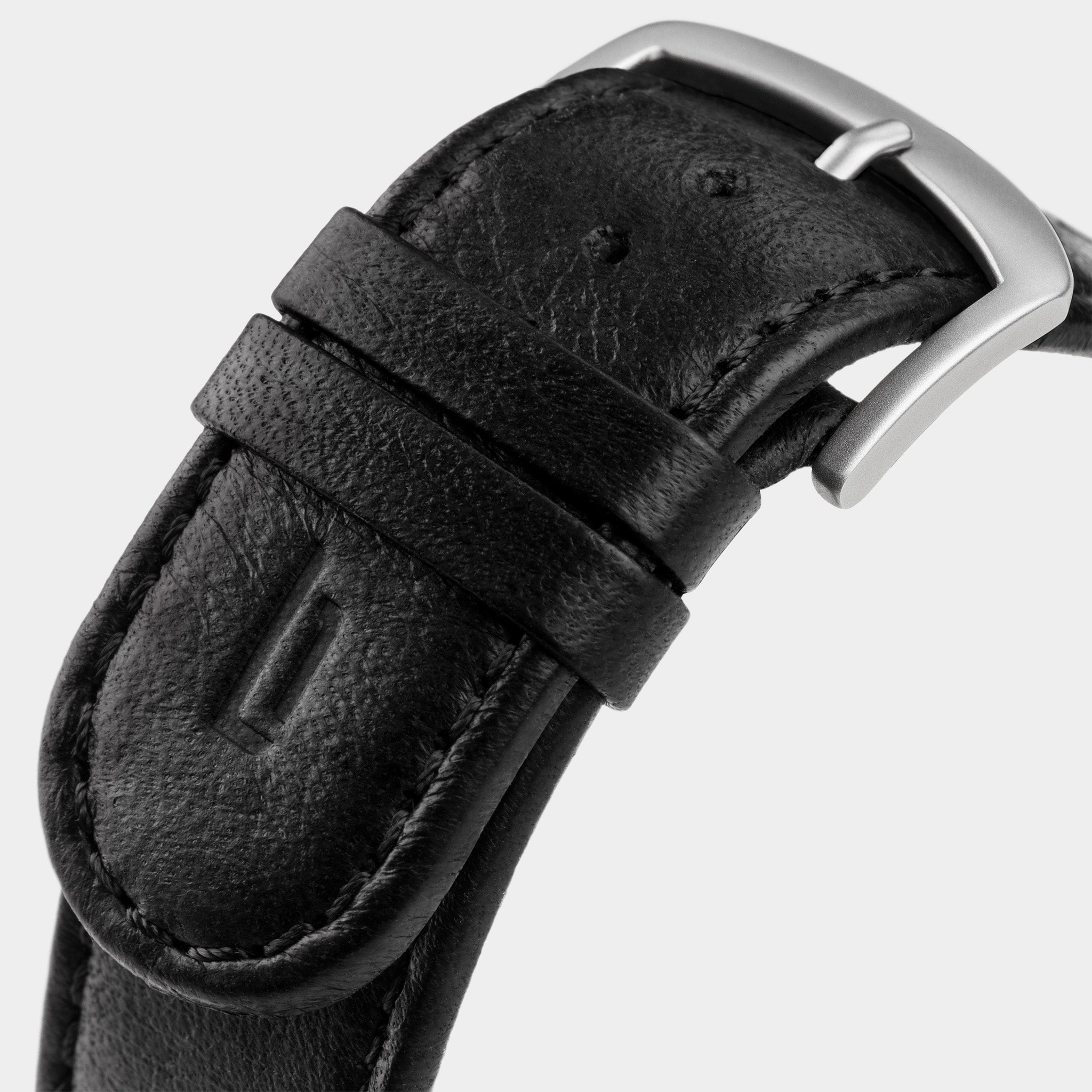 Close-up of a black leather watch strap with a silver buckle on a light background