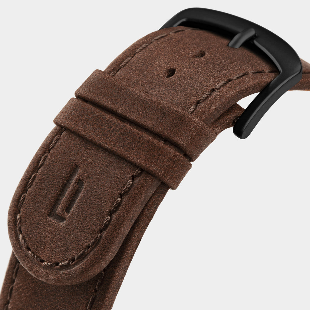 Close-up of brown leather watch strap with black metal buckle and detailed stitching