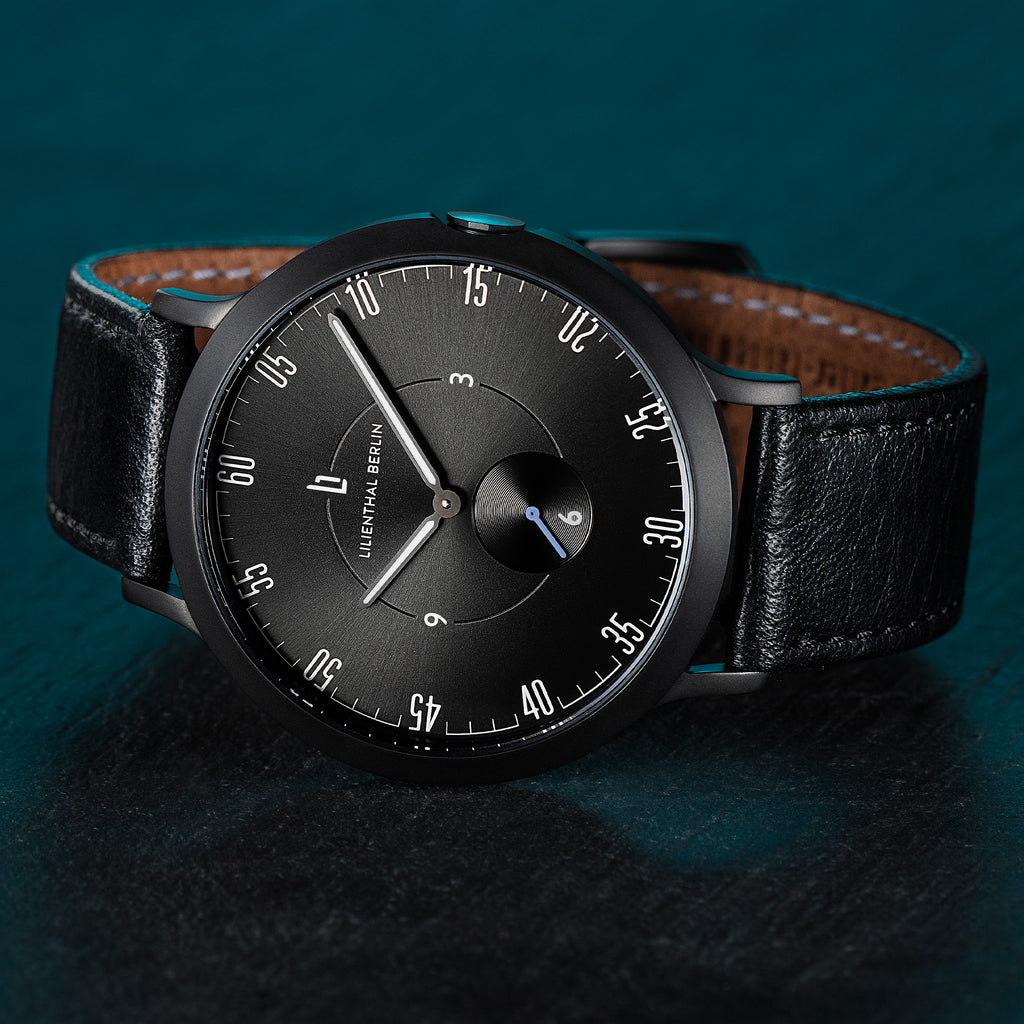 Minimalist black wristwatch with leather strap against dark textured background