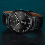 Minimalist black wristwatch with leather strap against dark textured background
