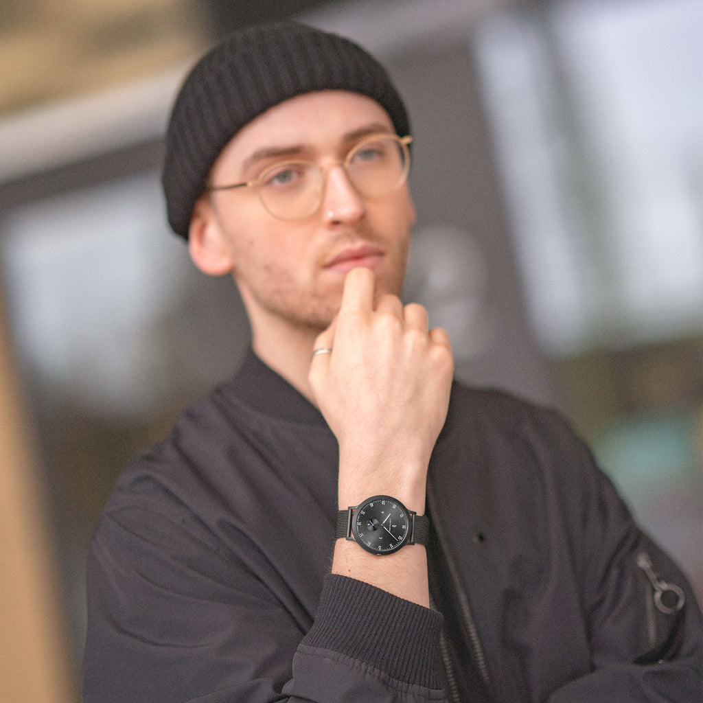Man wearing minimalist black wristwatch and black beanie, dressed in black jacket