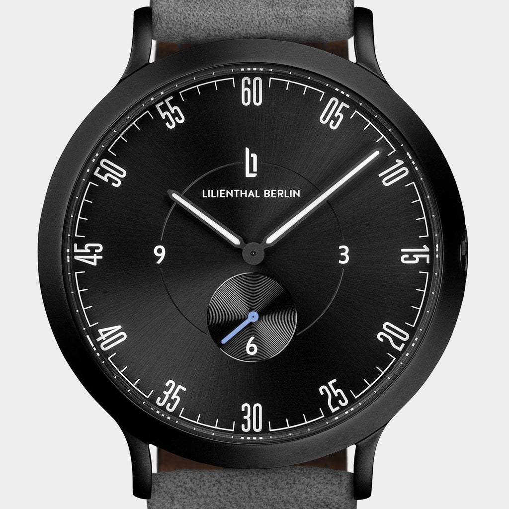Minimalist black analog watch with white markers, grey strap, subdial, and modern design.