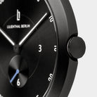 Close-up of a minimalist black men's wristwatch with white markers and a blue second hand