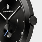 Close-up of a minimalist black men's wristwatch with white markers and a blue second hand