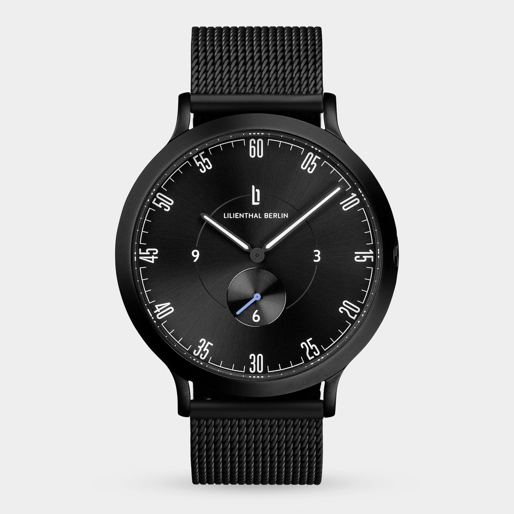 Minimalist black analog watch with mesh strap and sleek dial on white background